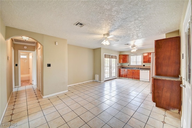 kitchen featuring arched walkways, light tile patterned floors, visible vents, brown cabinetry, and white dishwasher