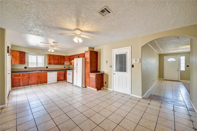 kitchen featuring arched walkways, light tile patterned flooring, white appliances, a sink, and visible vents