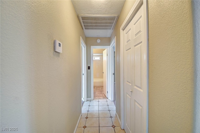 hall featuring visible vents, a textured wall, baseboards, and light tile patterned floors