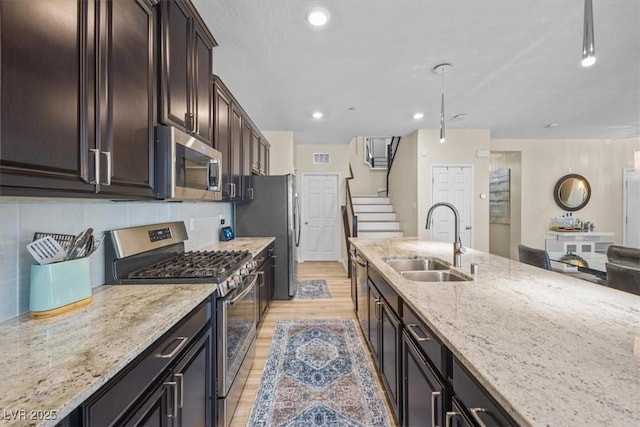 kitchen with light stone counters, decorative light fixtures, decorative backsplash, appliances with stainless steel finishes, and sink