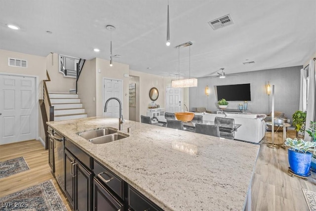 kitchen featuring light stone counters, pendant lighting, light wood-type flooring, ceiling fan, and sink