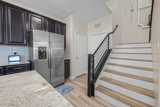 kitchen featuring light stone countertops, light hardwood / wood-style flooring, stainless steel fridge with ice dispenser, tasteful backsplash, and dark brown cabinets