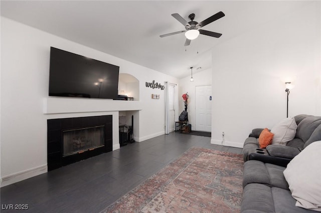 living room featuring ceiling fan, dark wood-type flooring, a tile fireplace, and vaulted ceiling