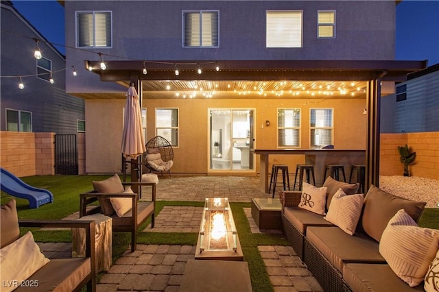 back house at night with an outdoor living space with a fire pit, a bar, and a patio area