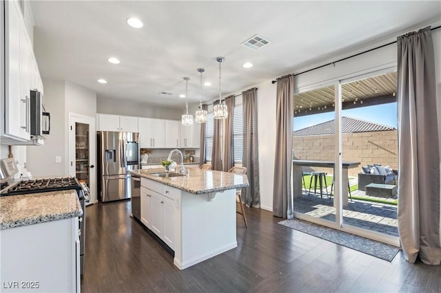 kitchen featuring a center island with sink, stainless steel appliances, hanging light fixtures, sink, and white cabinetry