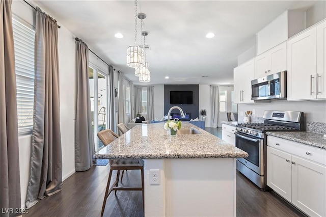 kitchen featuring sink, white cabinets, a kitchen bar, a kitchen island with sink, and appliances with stainless steel finishes