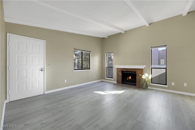 unfurnished living room with a brick fireplace, beam ceiling, and light hardwood / wood-style floors