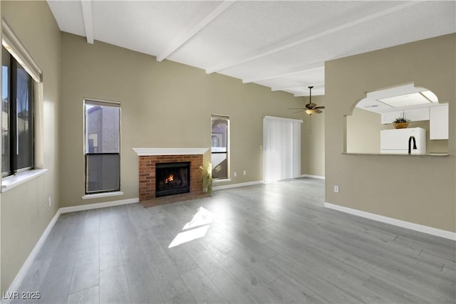 unfurnished living room featuring a brick fireplace, ceiling fan, plenty of natural light, and light wood-type flooring