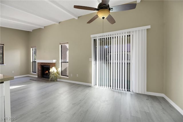 unfurnished living room featuring a fireplace, ceiling fan, light hardwood / wood-style flooring, and beamed ceiling