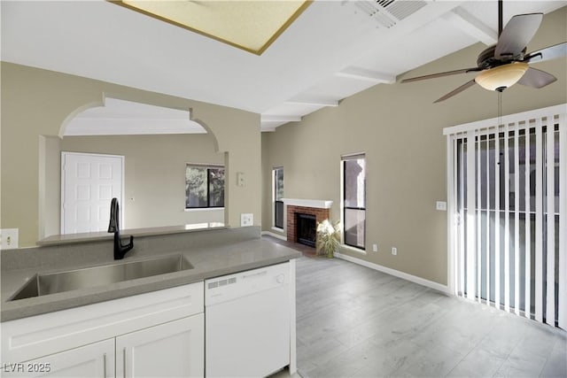 kitchen featuring vaulted ceiling with beams, white dishwasher, a brick fireplace, sink, and white cabinetry