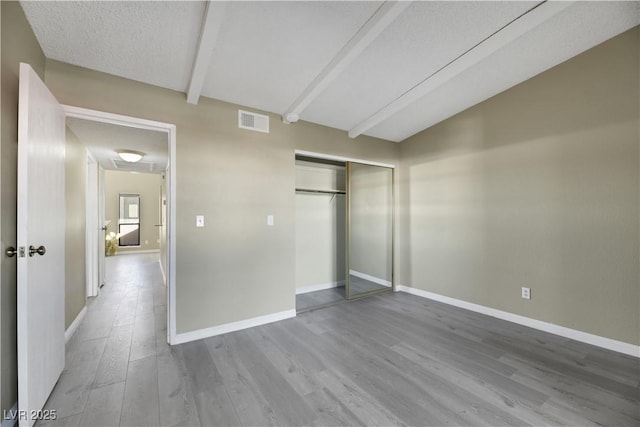 unfurnished bedroom with a textured ceiling, hardwood / wood-style flooring, a closet, and vaulted ceiling with beams