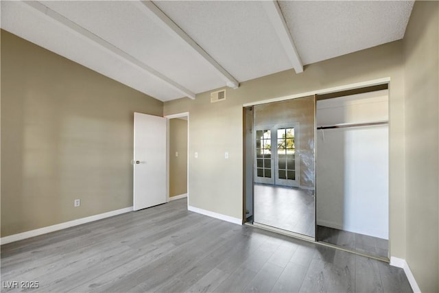 unfurnished bedroom featuring a closet, lofted ceiling with beams, a textured ceiling, and light wood-type flooring