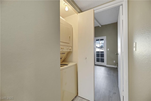 laundry room featuring stacked washer and clothes dryer, light wood-type flooring, and a textured ceiling