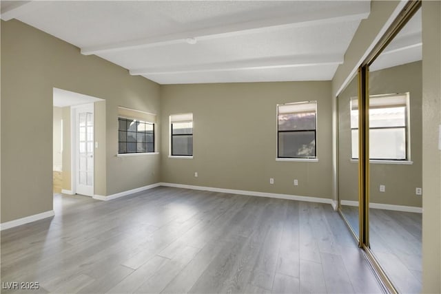 spare room with lofted ceiling with beams, plenty of natural light, and wood-type flooring