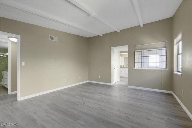 spare room featuring light hardwood / wood-style floors and beam ceiling