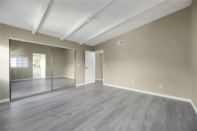 unfurnished bedroom with a textured ceiling, a closet, lofted ceiling with beams, and light hardwood / wood-style floors