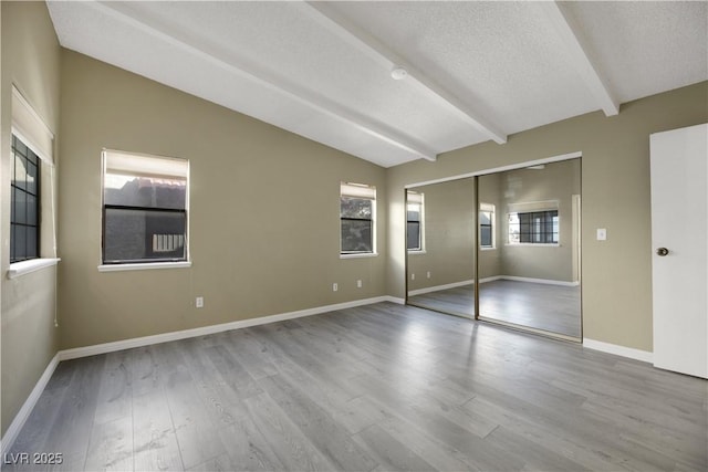 unfurnished bedroom featuring a textured ceiling, a closet, light hardwood / wood-style flooring, and vaulted ceiling with beams