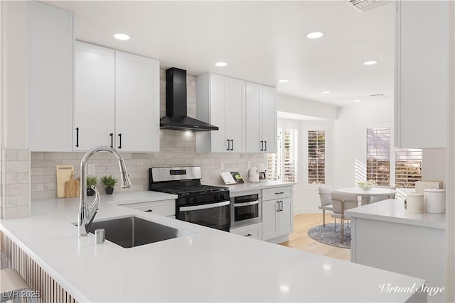 kitchen featuring stainless steel appliances, wall chimney range hood, white cabinets, and sink