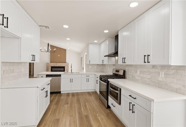 kitchen featuring stainless steel appliances, sink, white cabinetry, kitchen peninsula, and wall chimney range hood