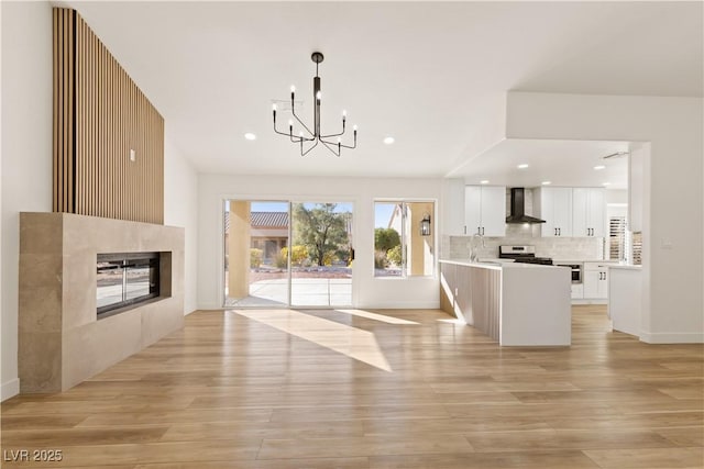 kitchen featuring white cabinetry, stainless steel stove, wall chimney exhaust hood, a multi sided fireplace, and hanging light fixtures