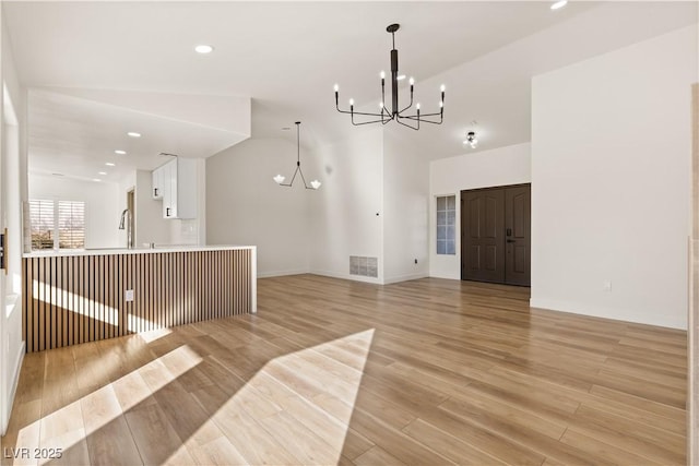 interior space featuring white cabinets, decorative light fixtures, lofted ceiling, light hardwood / wood-style flooring, and a notable chandelier