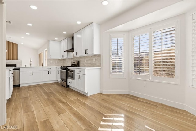 kitchen with appliances with stainless steel finishes, wall chimney exhaust hood, light hardwood / wood-style floors, and white cabinetry