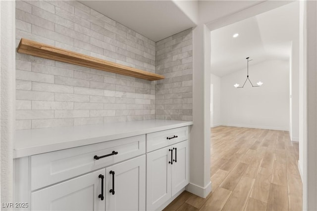 kitchen featuring decorative light fixtures, white cabinetry, lofted ceiling, light hardwood / wood-style flooring, and a notable chandelier