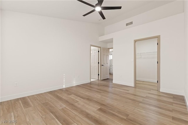 unfurnished bedroom with ceiling fan, a walk in closet, light wood-type flooring, and a closet