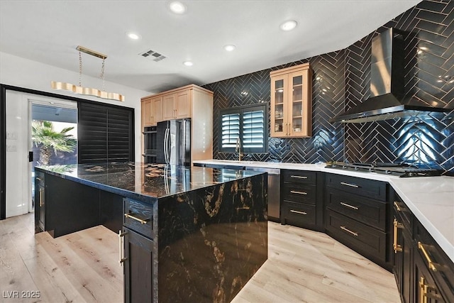 kitchen featuring wall chimney exhaust hood, light hardwood / wood-style flooring, a center island, tasteful backsplash, and appliances with stainless steel finishes