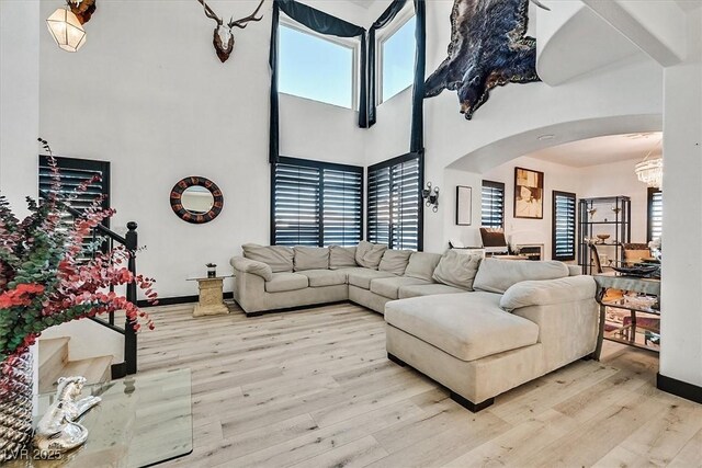 living room with a high ceiling, an inviting chandelier, light hardwood / wood-style flooring, and a wealth of natural light