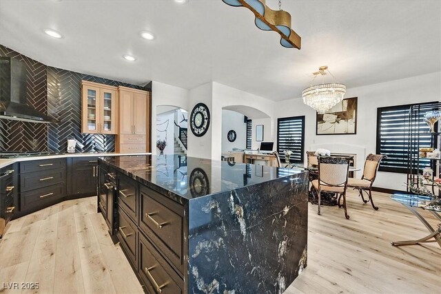 kitchen with an inviting chandelier, wall chimney exhaust hood, light hardwood / wood-style floors, a kitchen island, and pendant lighting