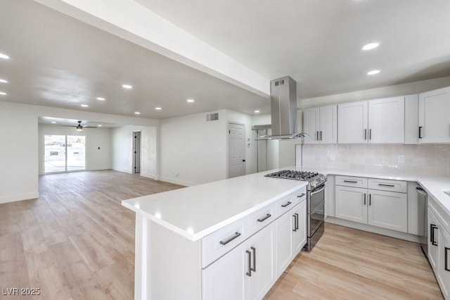 kitchen featuring stainless steel appliances, ceiling fan, island exhaust hood, kitchen peninsula, and backsplash