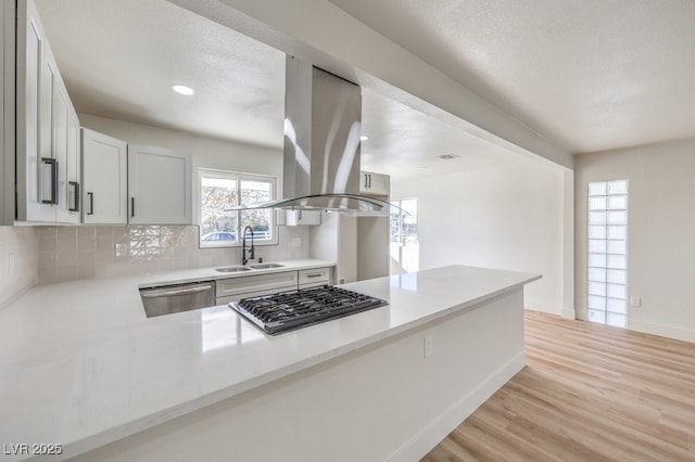 kitchen with kitchen peninsula, island exhaust hood, white cabinetry, appliances with stainless steel finishes, and sink