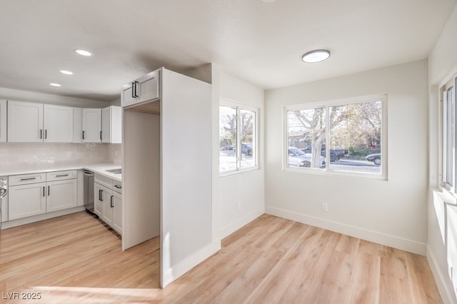 kitchen with dishwasher, white cabinetry, backsplash, and light hardwood / wood-style flooring