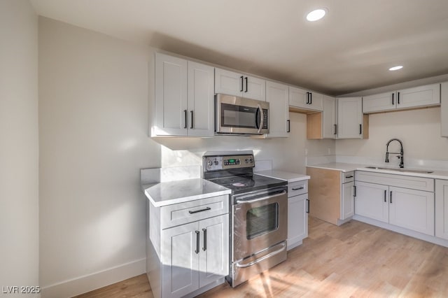 kitchen featuring white cabinets, light wood-type flooring, appliances with stainless steel finishes, and sink