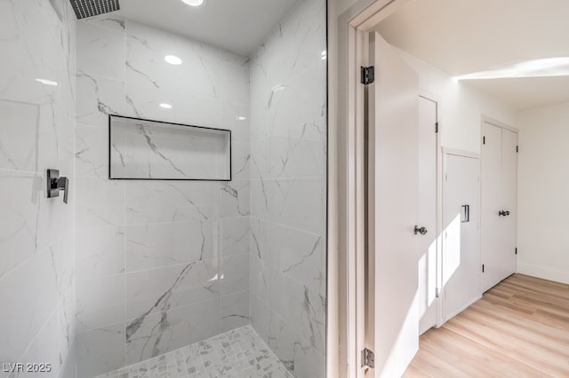 bathroom with a tile shower and hardwood / wood-style floors