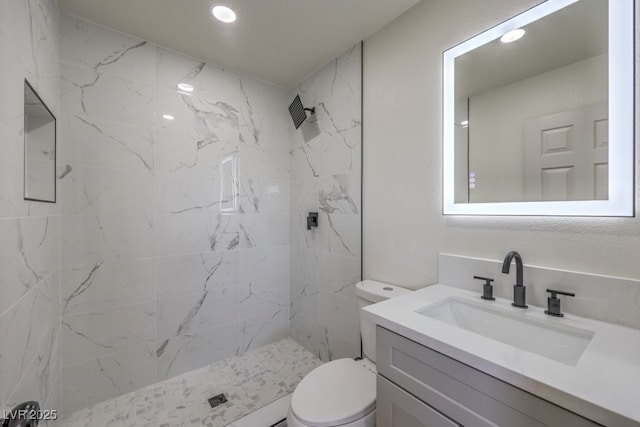 bathroom featuring a tile shower, vanity, and toilet