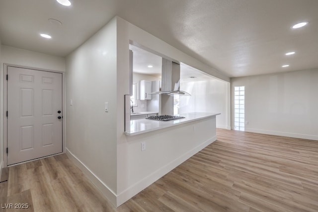 kitchen with kitchen peninsula, island exhaust hood, light wood-type flooring, stainless steel gas stovetop, and white cabinets