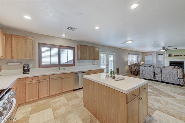 kitchen featuring tile counters, appliances with stainless steel finishes, a fireplace, light brown cabinets, and sink