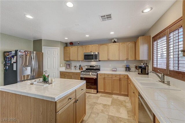 kitchen with stainless steel appliances, light brown cabinetry, tile countertops, and a center island