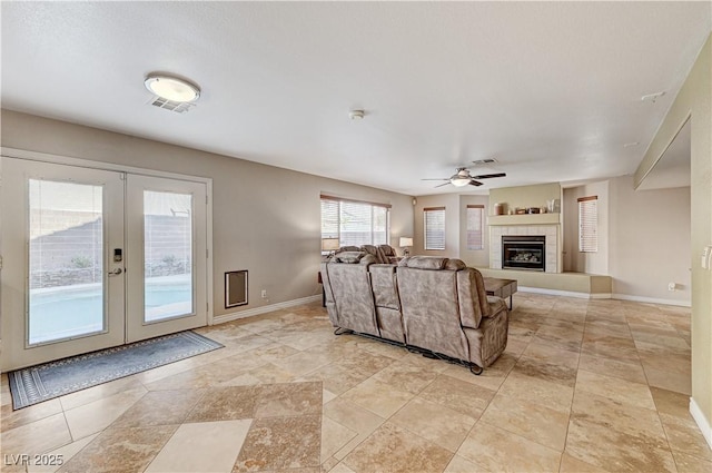 living room with a tile fireplace, ceiling fan, and french doors