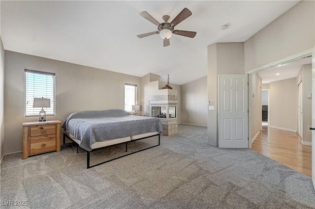 bedroom featuring lofted ceiling, a tiled fireplace, light carpet, and ceiling fan