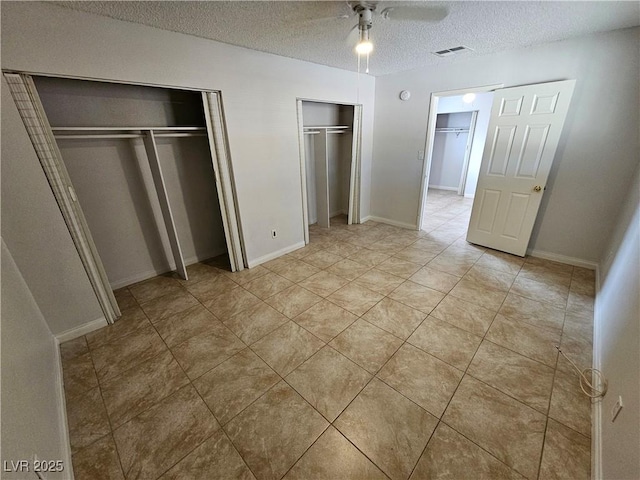 unfurnished bedroom with multiple closets, ceiling fan, a textured ceiling, and light tile patterned floors