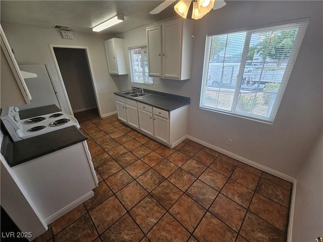 kitchen featuring stovetop, ceiling fan, dark tile patterned flooring, white cabinets, and sink