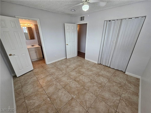 unfurnished bedroom featuring ceiling fan, a textured ceiling, sink, ensuite bathroom, and light tile patterned flooring