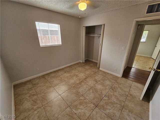 unfurnished bedroom with ceiling fan, a closet, light tile patterned flooring, and a textured ceiling