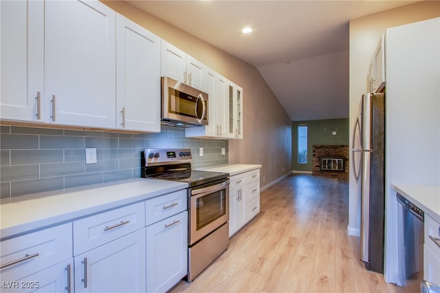 kitchen with vaulted ceiling, appliances with stainless steel finishes, a fireplace, white cabinets, and light hardwood / wood-style flooring