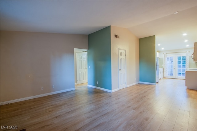 empty room with light wood-type flooring, french doors, and vaulted ceiling