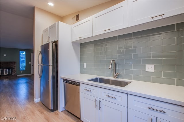 kitchen featuring light hardwood / wood-style floors, decorative backsplash, white cabinets, appliances with stainless steel finishes, and sink