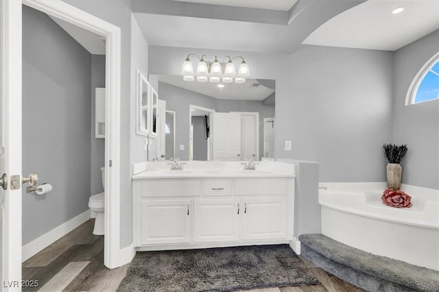 bathroom with hardwood / wood-style floors, a tub, vanity, and toilet